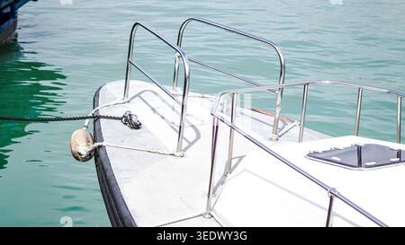 The bow of a white boat with chrome railings moored in turquoise water Stock Photo