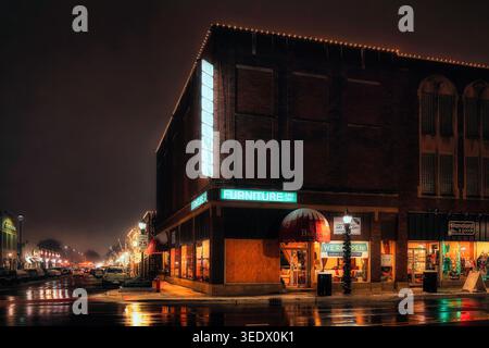 Historic Beidelman Furniture building at night with glowing neon signs and holiday lights reflecting on wet pavement in downtown Naperville Illinois Stock Photo