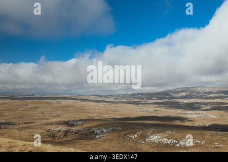 Wide panoramic mountain landscape with dramatic cloud formations and rolling grass-covered hills under bright blue sky. Stock Photo