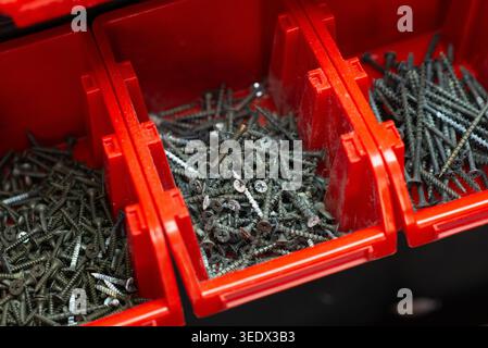 Various metal screws organized in red plastic storage bins in a workshop, close-up view. Stock Photo