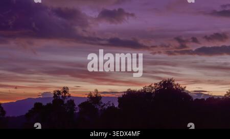 The last light of the sun gives the sky a deep purple tone, over the forests and farms of the eastern Andean mountain of central Colombia Stock Photo
