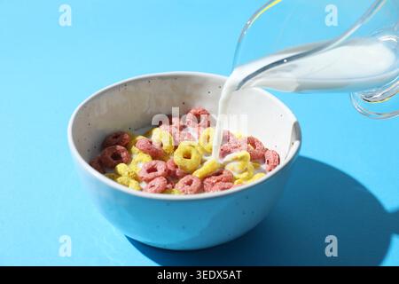 Pouring milk into bowl of delicious cereal on light blue background, closeup Stock Photo