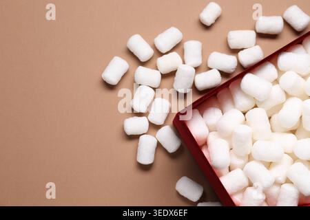 Gift box with packing peanuts on brown background, flat lay. Space for text Stock Photo