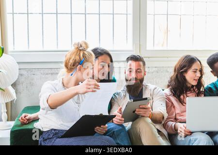 Diverse group of students working together on a project, analyzing documents and using digital devices Stock Photo