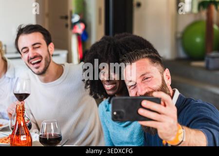 Diverse friends laughing and taking a selfie at a home dinner party with wine Stock Photo