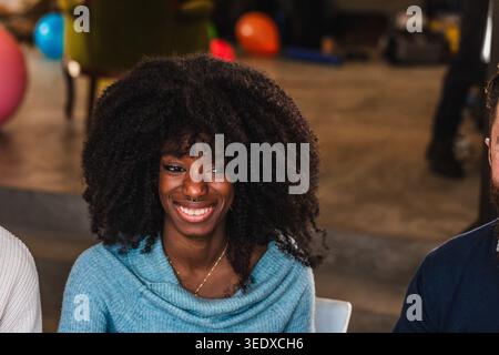 Young woman with afro hair smiling and enjoying a casual indoor party Stock Photo