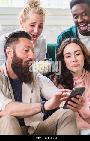 Happy young people resting on sofa, watching funny content on phone during leisure time Stock Photo