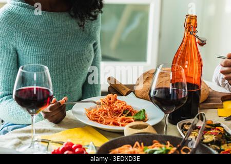 Woman eating italian spaghetti pasta, enjoying a casual home meal with red wine Stock Photo