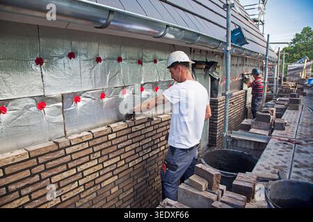 Netherlands, bricklayers are building the outer wall of a new house. Insulation foil is located between the inner and outer walls. Stock Photo
