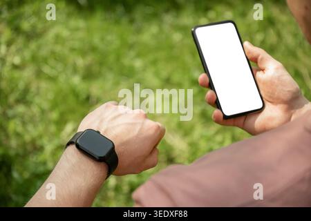 Man using smartphone and smartwatch mockup outdoors in sunny park Stock Photo