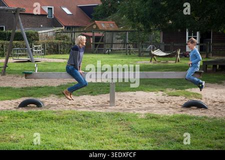 Netherlands, mother and sun on a teeter-totter or seesaw. Because the mother has double the weight of her son she sits halfway to keep the seesaw in b Stock Photo