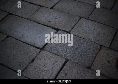 Close-up of a classic dark grey cobblestone pavement made of rectangular granite blocks. Traditional urban street texture. Stock Photo