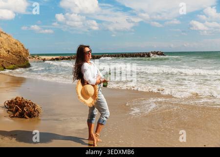 Laughing woman on beach holding reusable bottle and straw hat Stock Photo