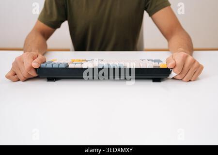 Cropped shot of male hands holding modern mechanical keyboard with colorful keycaps, showcasing technology, coding, setup for gaming, remote work Stock Photo