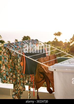 Laundry and beachwear drying on a balcony rack at sunset. Cozy travel lifestyle scene with tropical background, sunlight, vacation mood, and eco-frien Stock Photo
