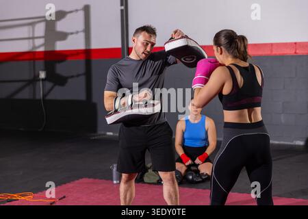 Coach in sportswear holding focus mitts and trainee punching with bright pink gloves on red mat. Trainer, boxing, gym, padwork, shadow, ring, cinderbl Stock Photo