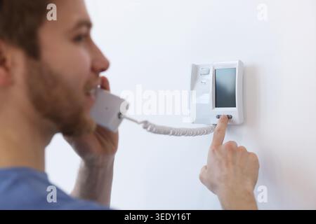 Man with handset pressing button on intercom panel indoors, closeup Stock Photo