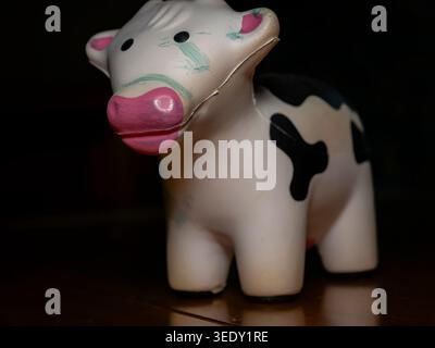 Close up view of a small black and white spotted toy cow with pink nose and green markings on its face sitting on a dark wooden surface Stock Photo
