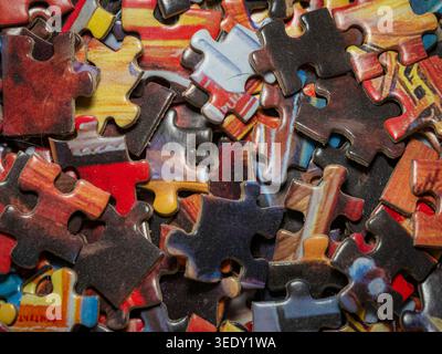 Top down macro view of a scattered pile of multi-colored jigsaw puzzle pieces with intricate details and textures in a messy arrangement Stock Photo