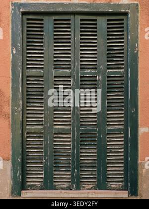 Old green shutters with peeling paint on a warm facade in Mallorca, detailed texture and Mediterranean character. copyspace. Stock Photo