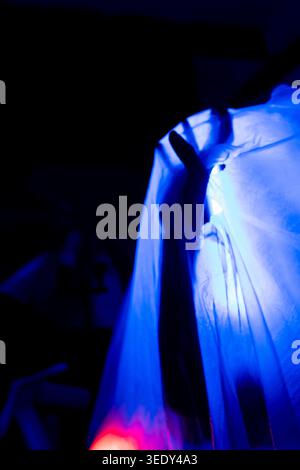 Minimal dark silhouette of a hand pressing through white translucent fabric under blue neon lighting. Conceptual horror and emotional isolation scene Stock Photo