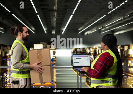 Male employee checking parcel status on a tracking software with tablet, shipment details and AWB tags ensuring package tracking in warehouse. Adult man wearing safety vest on platform. Stock Photo