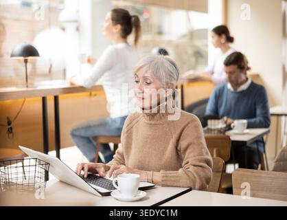 Confident senior female cafe customer enjoying peace and quiet while working on laptop Stock Photo