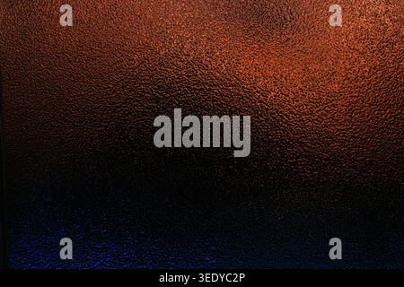 Dark frosted glass texture with a gradient fading from warm orange to deep blue Stock Photo