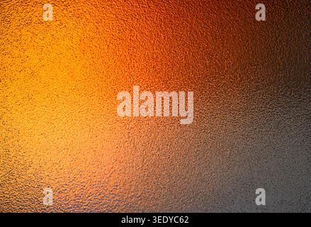 Warm orange and yellow light shining through textured privacy glass fading to dark grey Stock Photo