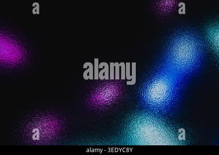 Defocused neon lights shining through dark textured frosted glass creating colorful bokeh Stock Photo