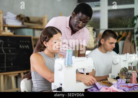 Middle-aged male teacher helping students sew Stock Photo
