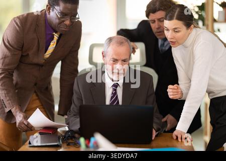 Group of businessmen working together, looking at a laptop and discussing issues Stock Photo