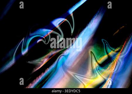 Neon blue, green, yellow and pink light trails sweep across a black background, forming fluid abstract shapes with glowing reflections, blur and iride Stock Photo