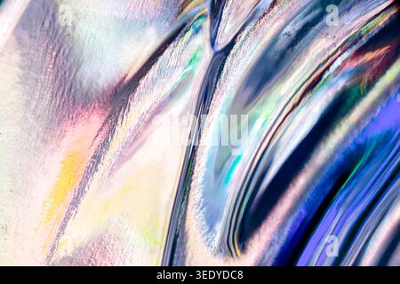 Pale iridescent streaks and glossy blue curves fill an abstract close-up, blending soft pink, yellow and cyan reflections with textured light patterns Stock Photo