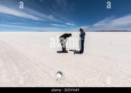 Two tourists examine hexagonal salt crust patterns on the vast Salar de Uyuni salt flat, Potosi, Bolivia, South America Stock Photo