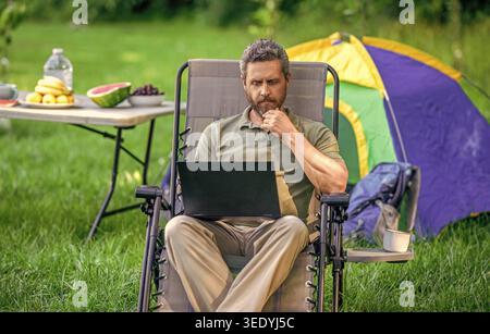 Businessman working outdoor. Man having camp picnic in forest with tent. Summer camping retreat. Business man typing on laptop at camping. Business Stock Photo