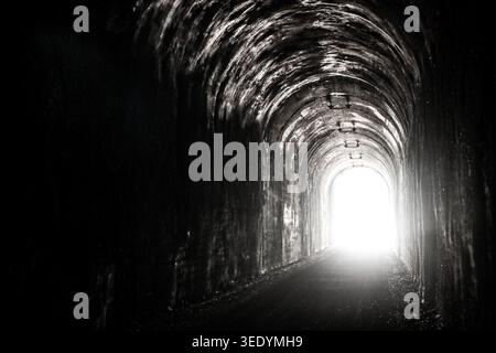 High Contrast Black and White Photography of Bright Sunlight at the End of a Dark Abandoned Railroad Tunnel Stock Photo