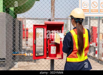 Professional woman inspector conducting a fire safety equipment audit and annual certification check at an outdoor factory site. Stock Photo