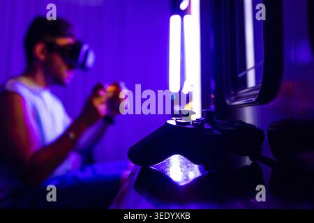 Close-up of a video game controller. In the background a man plays console with virtual reality goggles Stock Photo