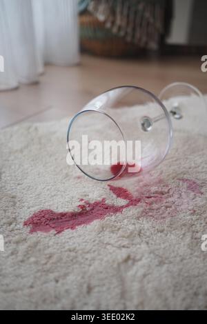 Red liquid spills from glass on rug in living room Stock Photo