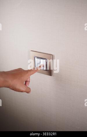 Hand pressing a light switch on a wall in a room Stock Photo