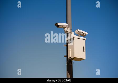 Two white CCTV surveillance cameras mounted on a gray pole against a clear blue sky background Stock Photo