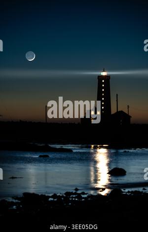 View of Grotta Lighthouse at night with a crescent moon in the dark sky and light reflecting on the water in Seltjarnarnes, Seltjarnarnesbaer, Iceland Stock Photo