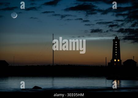 View of Grotta Lighthouse silhouetted against a twilight sky with a crescent moon and dark clouds over the water in Seltjarnarnes, Seltjarnarnesbaer, Stock Photo