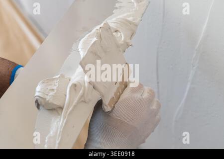 Skilled professional applying a smooth layer of plaster using a trowel on interior wall surface. Clean workspace with natural light enhancing the detail of the plastering process is visible. Stock Photo