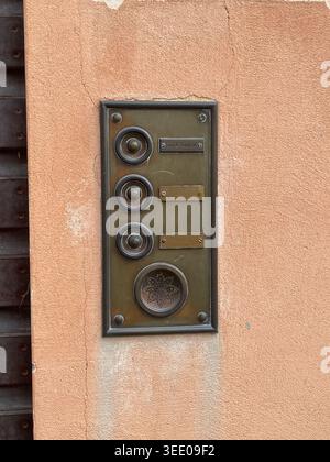 Ornate vintage brass doorbell and intercom panel mounted on a weathered peach stucco wall, showing aged patina, multiple buttons and speaker at a home Stock Photo