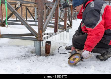 Worker using angle grinder on metal construction during winter outdoor repair work Stock Photo