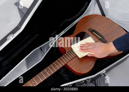 Person carefully cleaning the wooden body of an acoustic guitar with a soft microfiber cloth, performing instrument maintenance Stock Photo