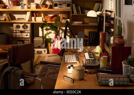 Wide shot of home music studio workspace featuring computer, microphone, keyboard, mixer, guitar, recording setup. Supporting podcast production, audio editing, creator branding Stock Photo