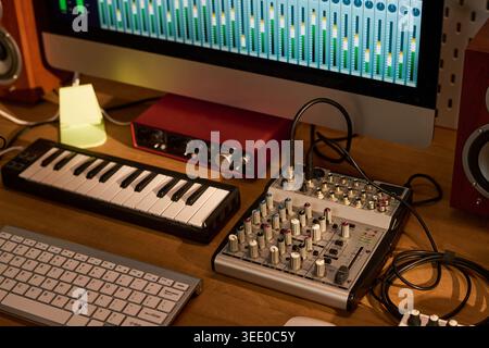 Close up of music production workstation showing computer audio mixer, MIDI keyboard, sound interface, studio controls. Supporting podcast editing, recording, sound design marketing Stock Photo